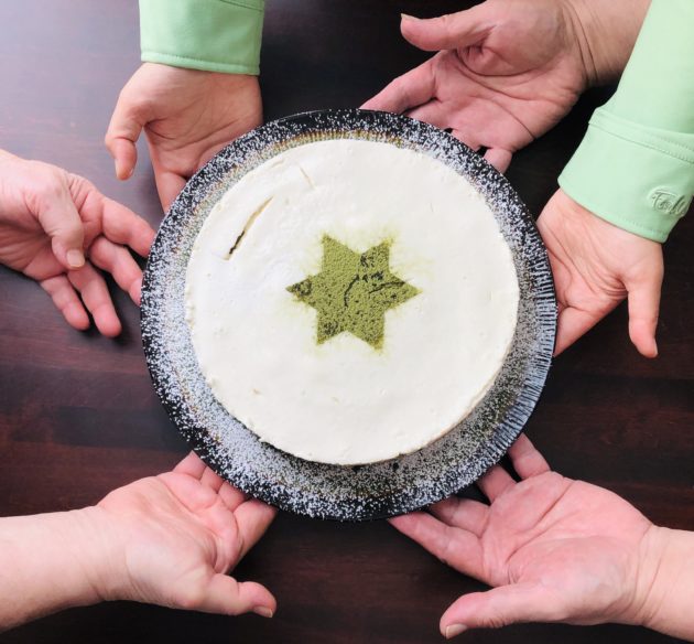 Matcha cheesecake with six hands holding it in a circle